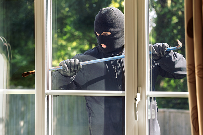 A masked burglar using a crowbar on a window.