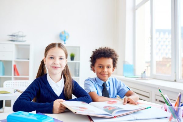 two children sitting in class, large window to the right.
